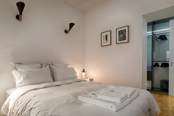 A neatly made bed with white linens, a bedside table with a lamp, and two framed pictures on the wall.