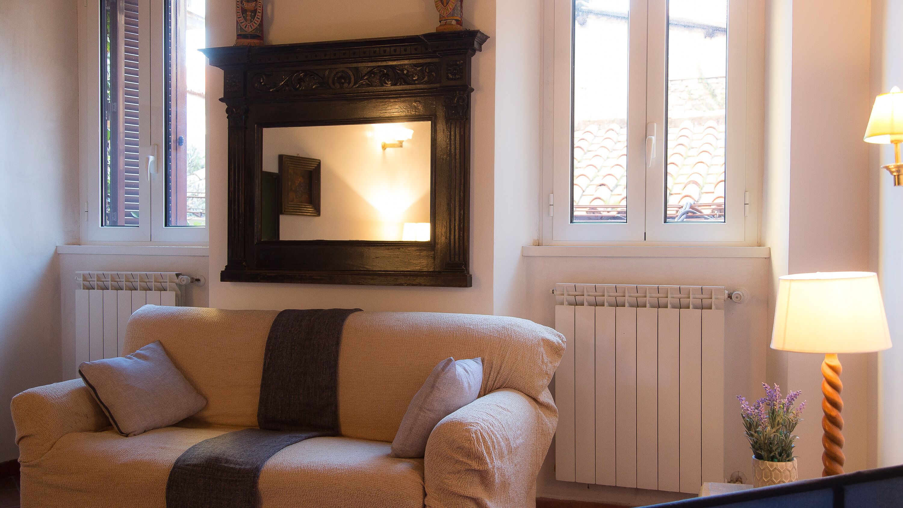 Una habitación acogedora con sofá, un espejo grande, un radiador y una lámpara.