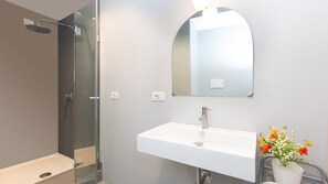 A modern bathroom with a glass shower enclosure, a white sink, and a mirror with a decorative light. - Arenula Apartment close to Piazza Navona (Rome)