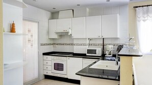 A compact kitchen with white cabinets, a microwave, an oven, and a sink. - La Rosaleda - Denia, Costa Blanca (Denia)