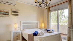 A hotel room with a bed, nightstands, and a balcony with a view of palm trees. - La Rosaleda - Denia, Costa Blanca (Denia)