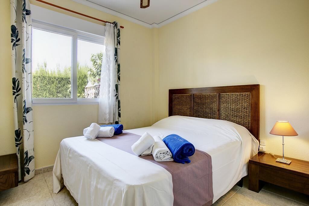 Une chambre d’hôtel avec deux lits, une fenêtre avec des rideaux, une tête de lit en bois et une lampe de chevet.