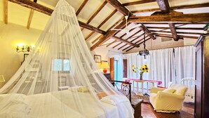 A bedroom with a canopy bed, a sitting area with a table and chairs, and a view of the outside. - Villa Elisa - Vacation rental with swimming pool near Cortona, Tuscany (Cortona)
