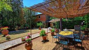 A patio with outdoor furniture, a table, and chairs under a woven shade. - Villa Elisa - Vacation rental with swimming pool near Cortona, Tuscany (Cortona)