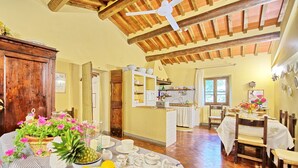 A spacious kitchen with wooden beams, a dining area with a table set for two, and a cozy living area with a fireplace. - Villa Elisa - Vacation rental with swimming pool near Cortona, Tuscany (Cortona)