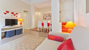 Ein modernes Wohnzimmer mit einer Couch, einem Fernseher und einem Essbereich mit Stühlen und einem Tisch.