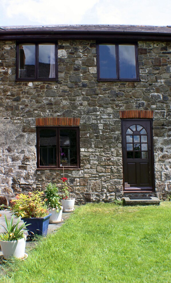 A stone building with two windows and a door, surrounded by a well-maintained lawn and potted plants.