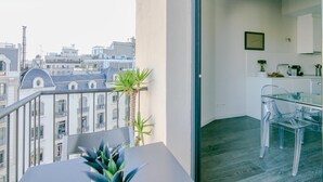 A balcony with a table and chairs, a potted plant, and a view of city buildings. - One bedroom apartment (Barcelona)