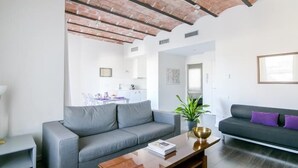 A modern living room with a grey sofa, a wooden coffee table, and a dark sofa with purple cushions. - One bedroom apartment (Barcelona)