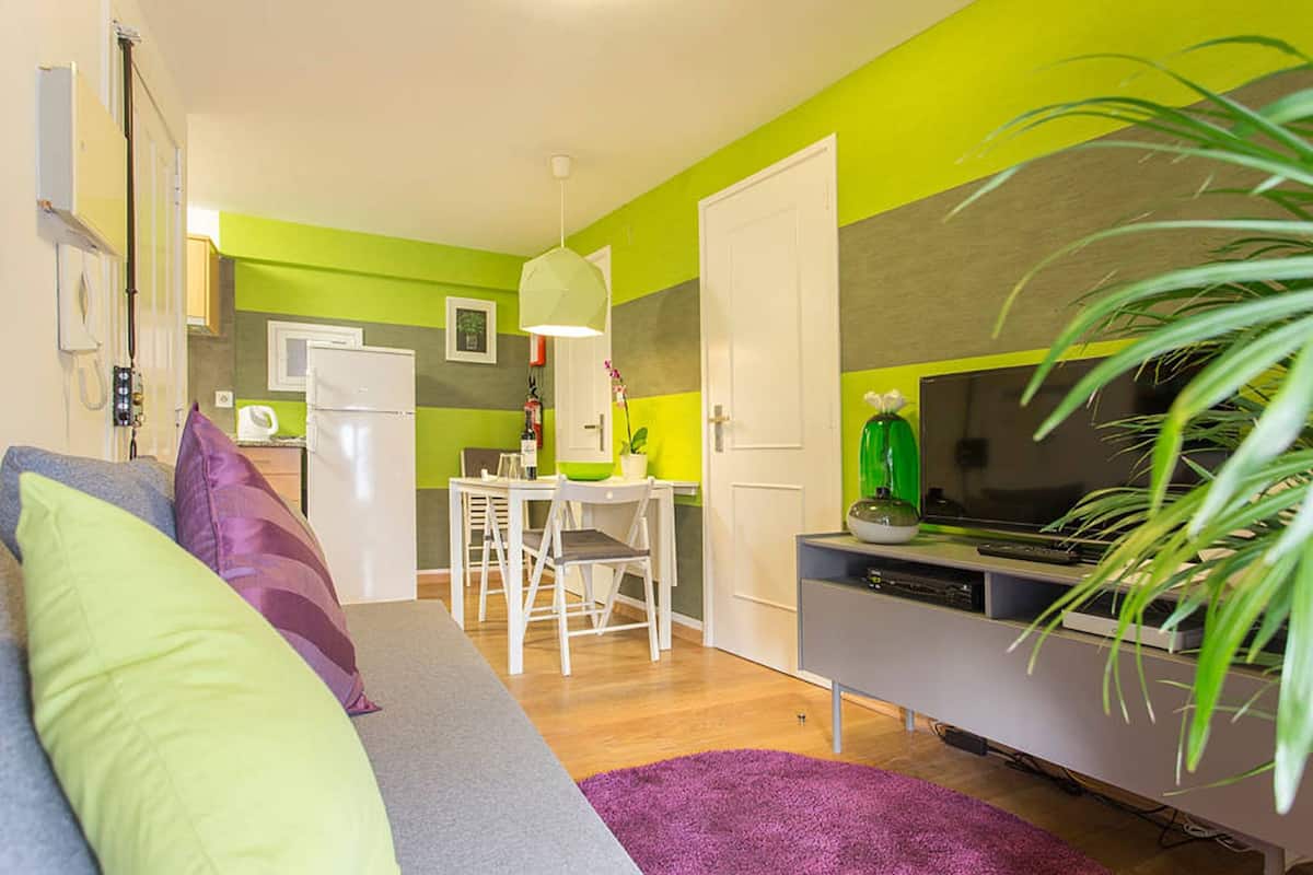 A modern living room with a grey sofa, a purple rug, and a TV stand with a flat-screen TV.