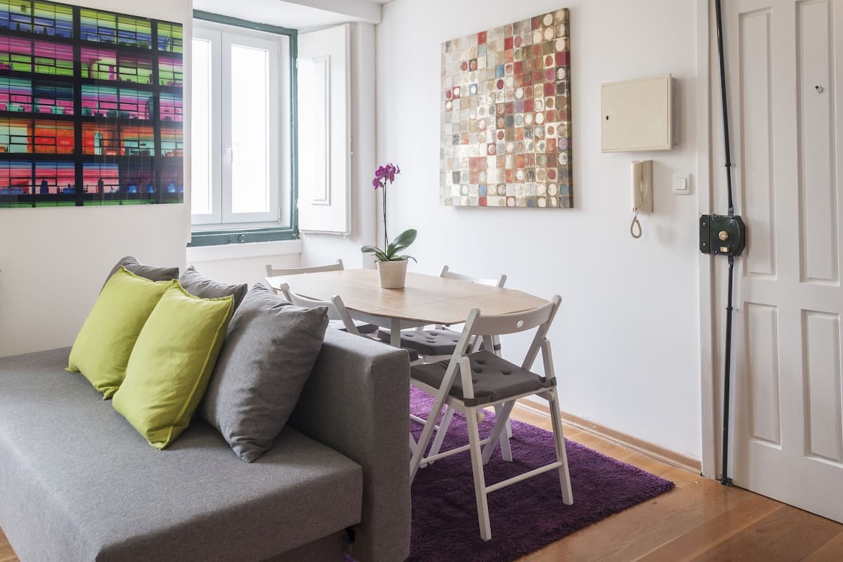 A modern living room with a gray sofa, a round wooden table, and a purple rug.