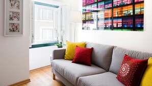A modern living room with a grey sofa, yellow and red cushions, a white lamp, and a colorful glass wall. - Contemporary by Apartments Alfama (Lisbon)
