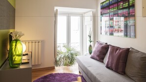 A modern living room with a grey sofa, a purple rug, a green vase with flowers, and a large window with a view of a balcony. - Contemporary by Apartments Alfama (Lisbon)