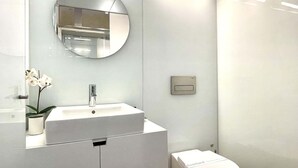 Une salle de bain moderne avec un lavabo blanc, un miroir rond, des toilettes et une petite orchidée en pot.