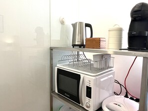 A kitchenette with a microwave, kettle, and coffee maker on a shelf.