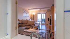 Amplia zona de estar con sofá, mesa de centro y televisor. Hay un ventanal corredero que da a un área exterior.