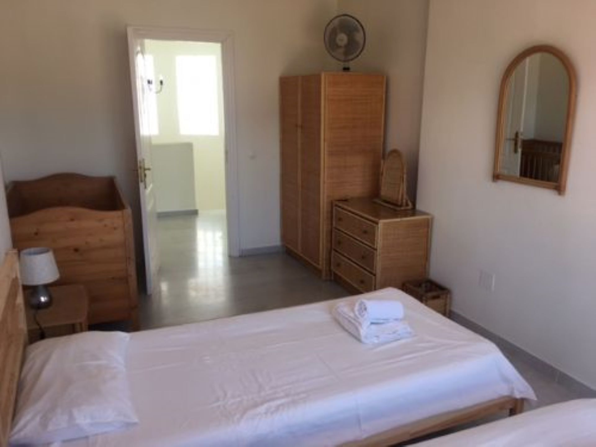 Une chambre à coucher avec un lit, une commode en bois, un miroir et un ventilateur.