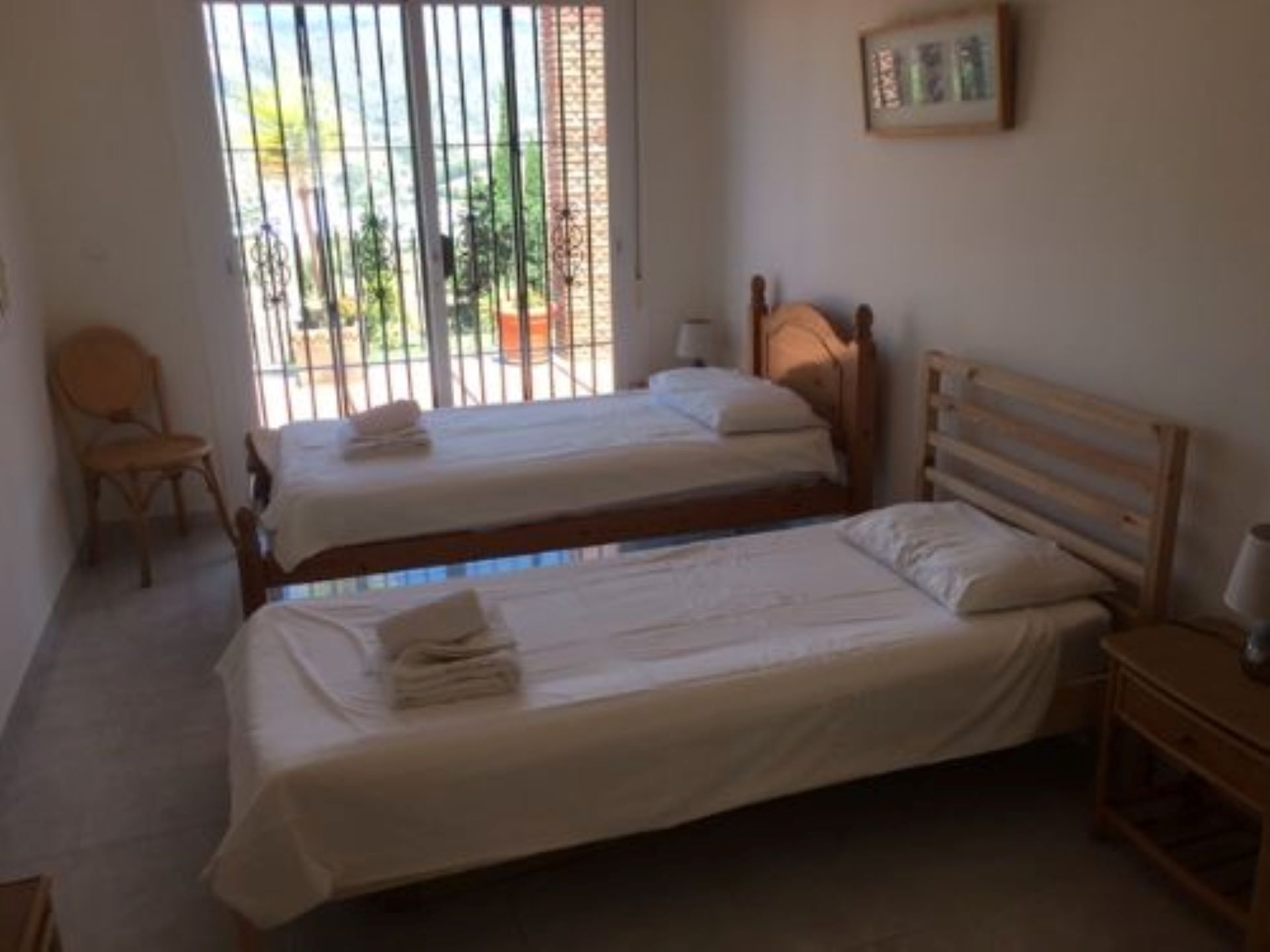 A room with two single beds, a wooden headboard, a chair, and a small table.