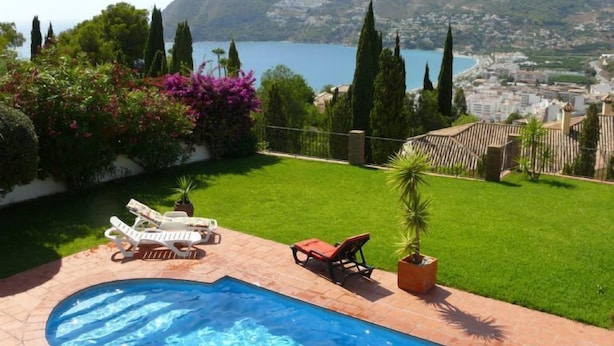 Un jardin avec une piscine, deux chaises longues et une vue sur une ville côtière.