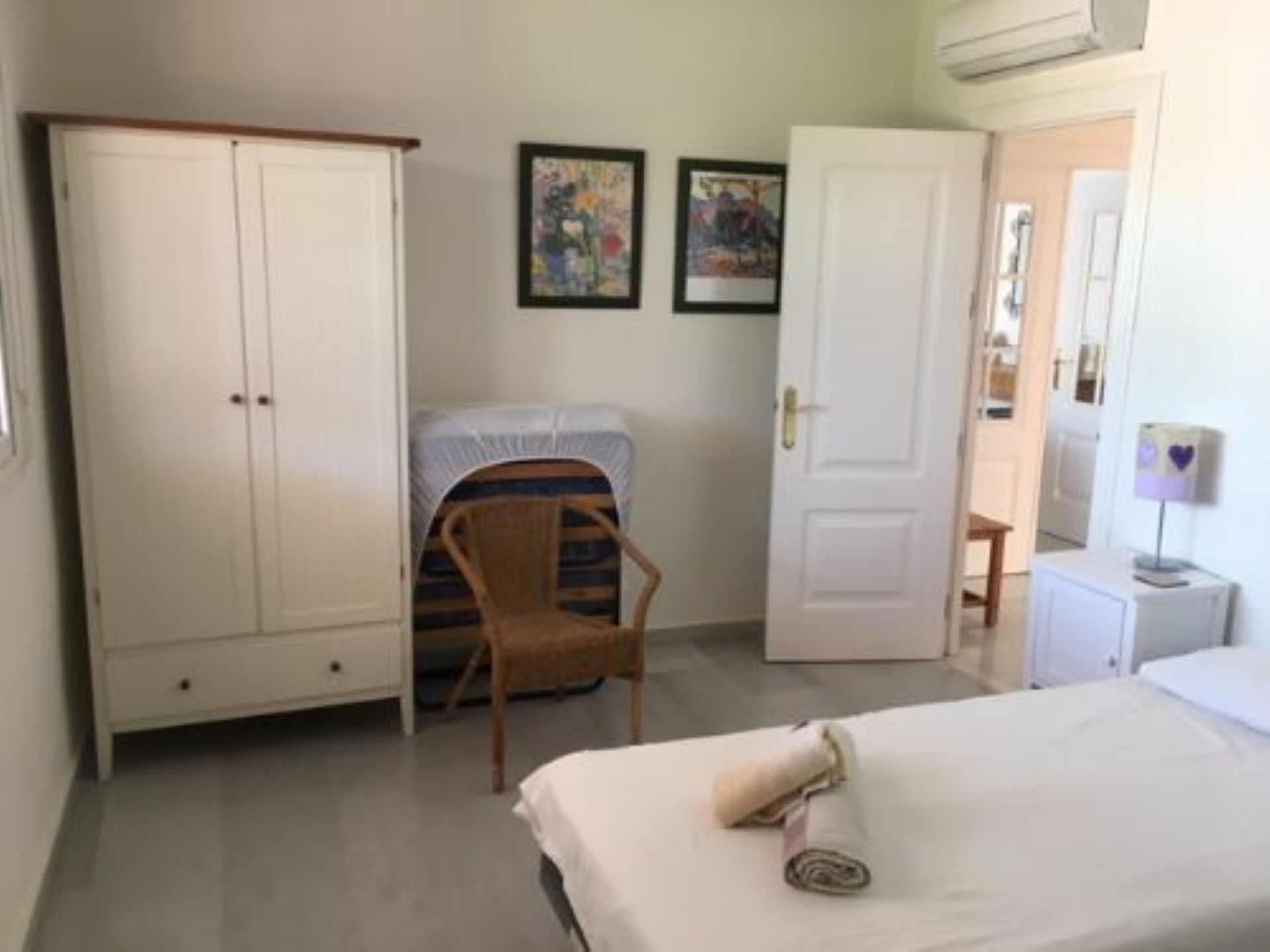 Ein Schlafzimmer mit einem Bett, einem Kleiderschrank, einem Sessel und zwei gerahmten Bildern an der Wand.