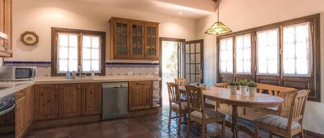 A kitchen with wooden cabinets, a dining table with chairs, and a hanging light fixture.