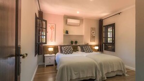 A bedroom with a bed, nightstands, an air conditioning unit, and a window with curtains. - Finca Horno de la Teja (Hornillo, El (Mogan))