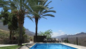 A swimming pool with a clear view of mountains in the background, surrounded by palm trees and lounge chairs. - Finca Horno de la Teja (Hornillo, El (Mogan))