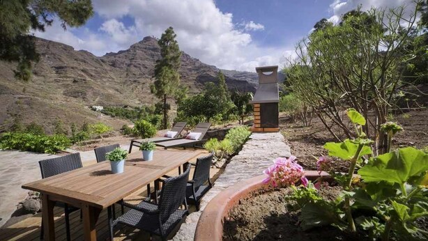 An outdoor patio with a wooden table and chairs, surrounded by potted plants and a stone pathway. - Finca Horno de la Teja (Hornillo, El (Mogan))