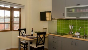 Une cuisine compacte avec un coin repas, une fenêtre donnant sur des immeubles et un pare-feu en carreaux verts.