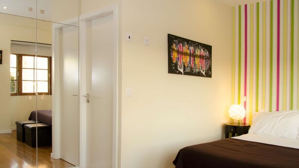 Une chambre à coucher avec un lit, une table de chevet, une lampe et un mur rayé aux couleurs vives.