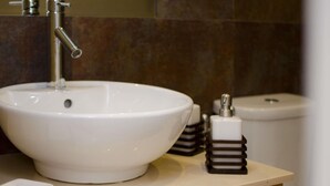 Une salle de bain avec un lavabo blanc, un robinet, des toilettes et un distributeur de savon posé sur le comptoir.