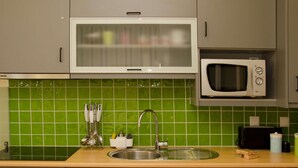Une cuisine avec un plan de travail recouvert de carreaux verts, un évier en acier inoxydable, un four à micro-ondes et un grille-pain.