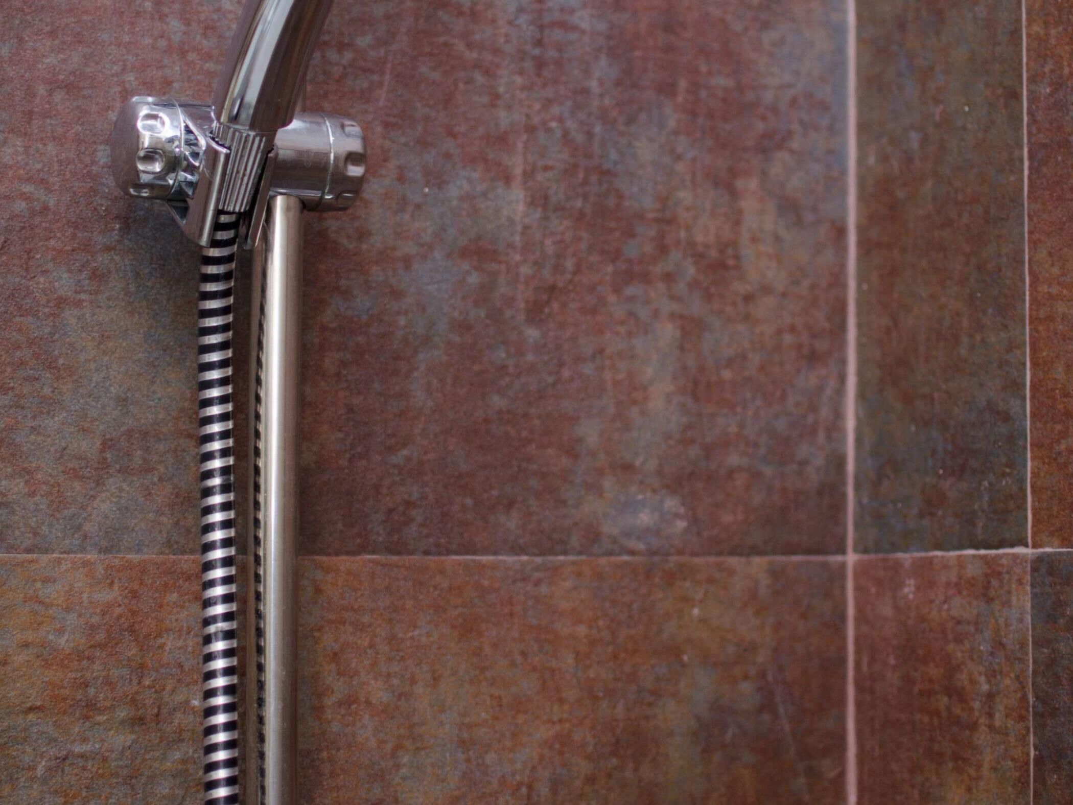 Un cabezal de ducha unido a una tubería de metal, probablemente parte de la fontanería de un baño.