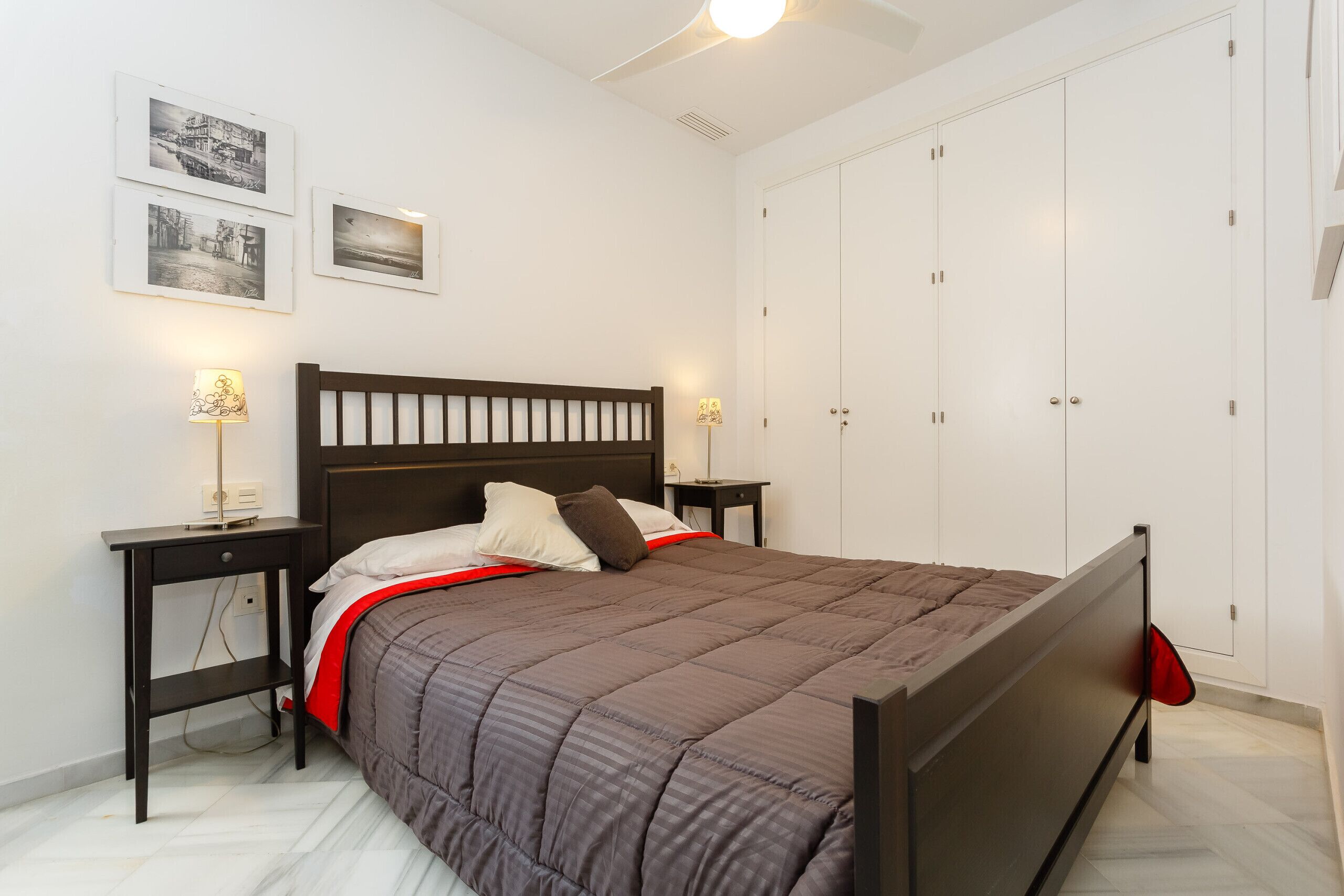 A bedroom with a bed, two bedside tables, a nightstand, a wardrobe, and three framed pictures on the wall.