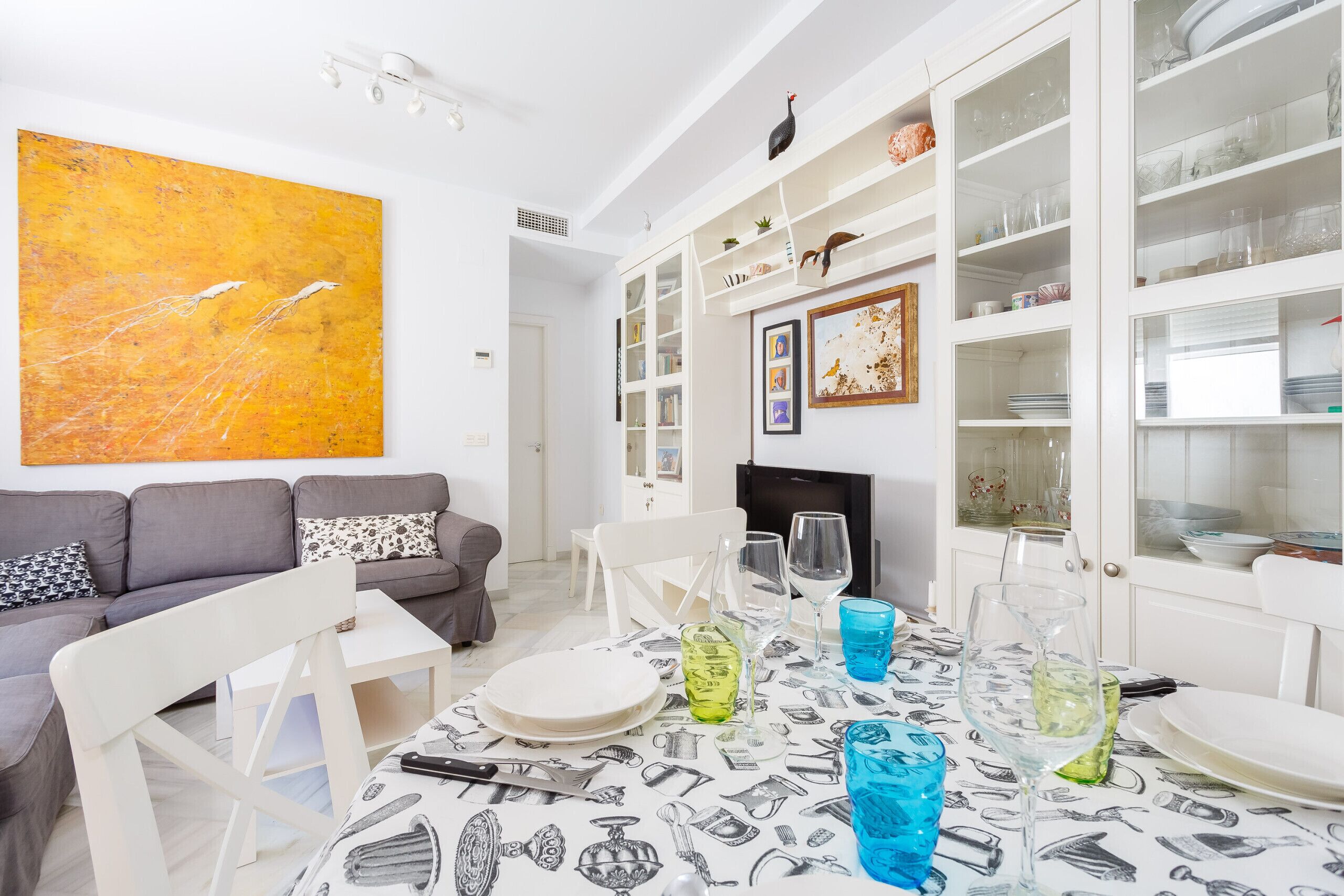 A dining area with a table set for four, white chairs, and a white cabinet with glass doors displaying dishes and glasses.