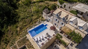 An aerial view of a property with a swimming pool, stone architecture, and a surrounding natural landscape.