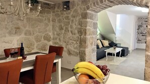 A dining area with a stone wall, a chandelier, and a table with a fruit bowl.