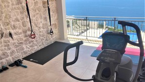 A home gym with a stationary bike, a yoga mat, and resistance bands against a stone wall.