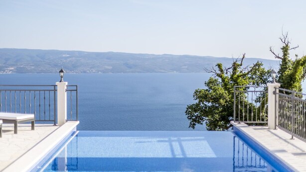 A pool with a view of the sea and distant hills.