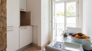 Una cocina luminosa con armarios blancos, una pared de acento de piedra, una mesa de comedor con un tazón de fruta y vistas al exterior a través de un ventanal grande.