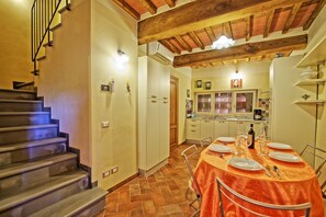 A dining area with a table set for four, a kitchen with a window, and a staircase leading to another level.