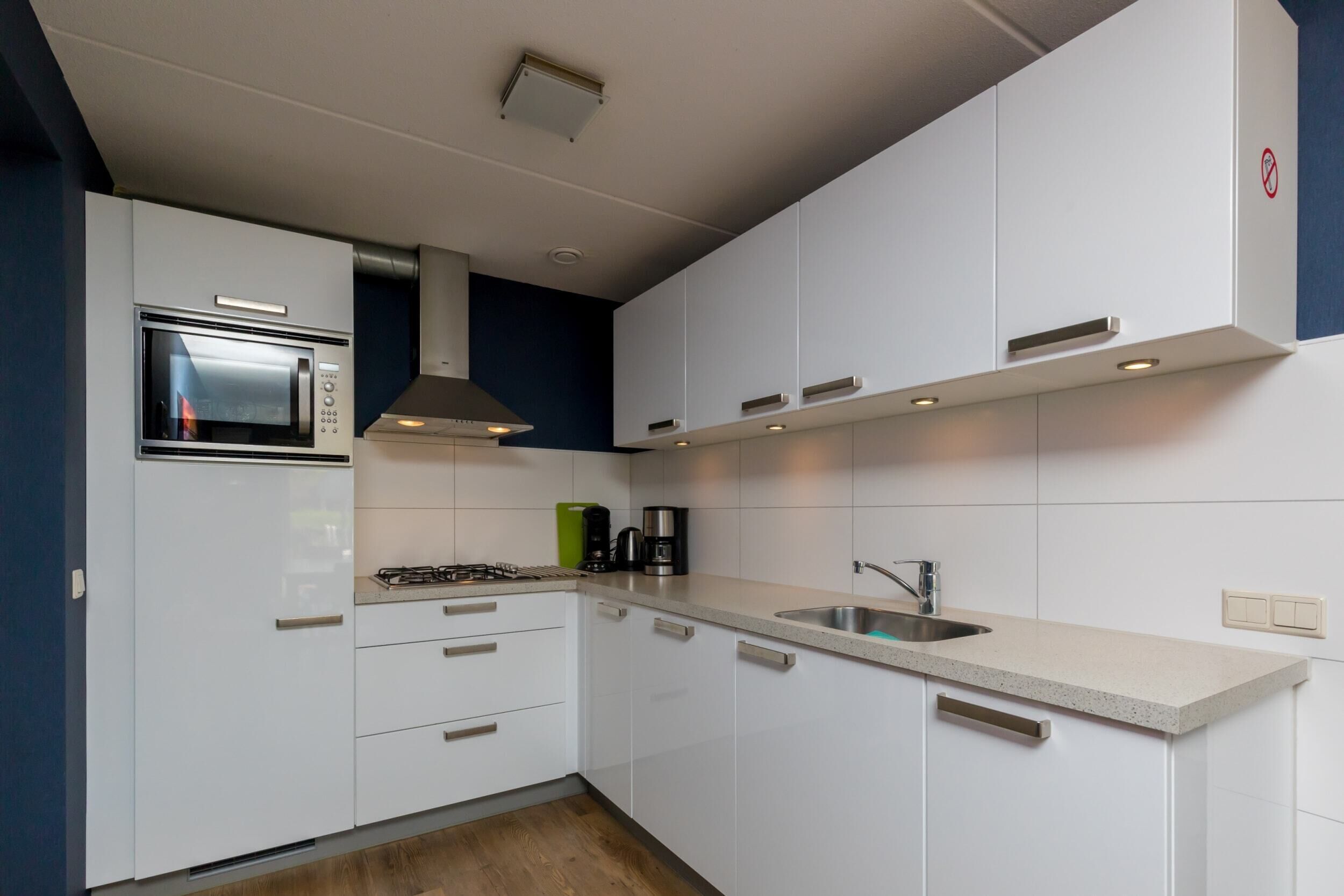 A modern kitchen with white cabinets, a built-in microwave, a gas stove, and a stainless steel sink.