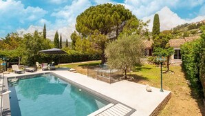 A swimming pool with lounge chairs and a pergola, surrounded by trees and a house with a tiled roof. - Villa in Callian with Heated Pool and Terrace (Callian)
