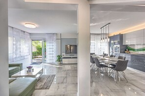 A modern kitchen with a dining area, large windows, and a view of the outdoors.