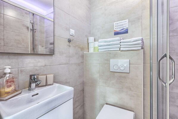 A modern bathroom with a glass shower enclosure, a sink with a soap dispenser, and a towel rack with neatly folded towels.
