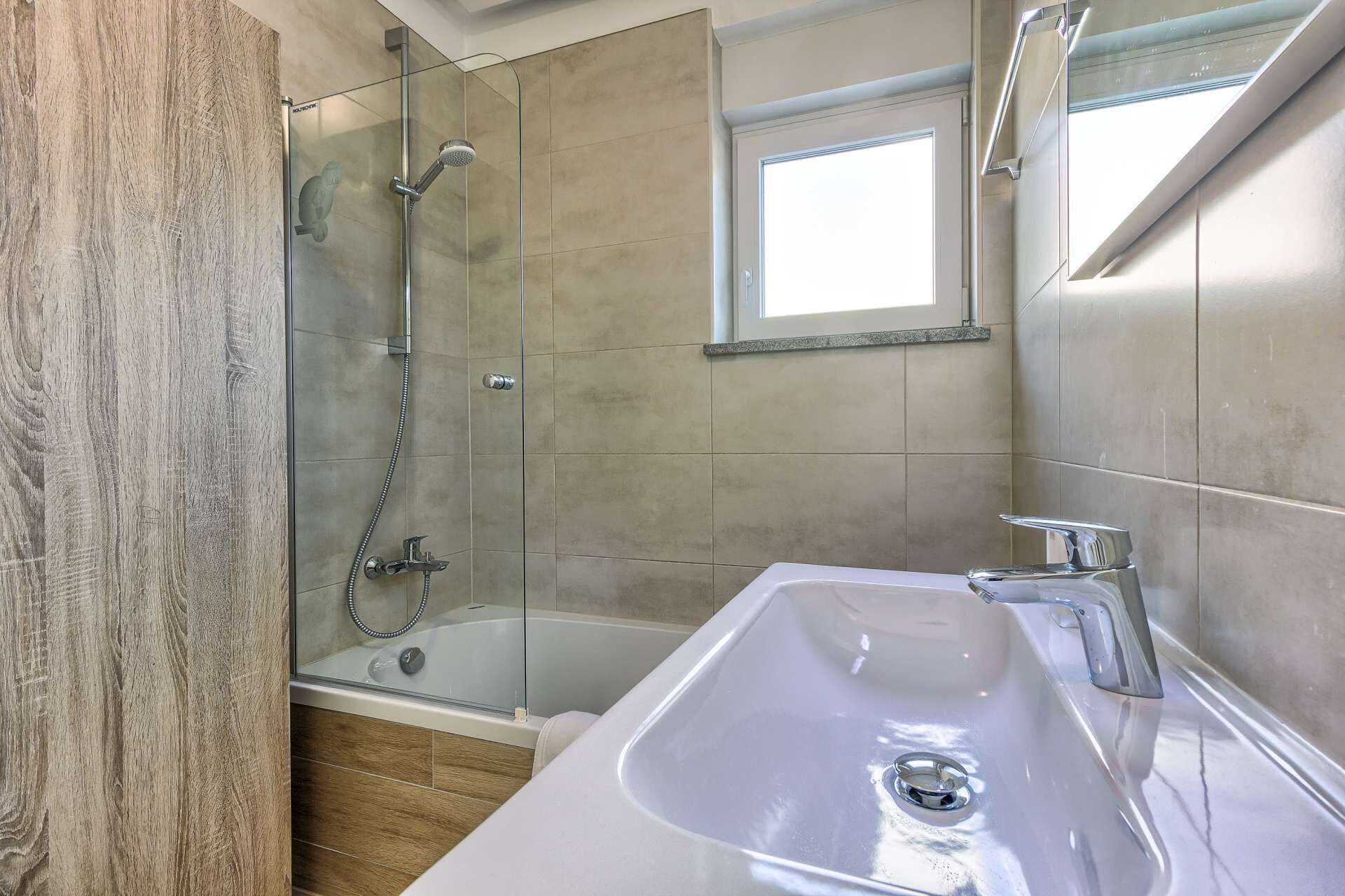 A modern bathroom with a glass-enclosed shower, a bathtub, and a large sink.