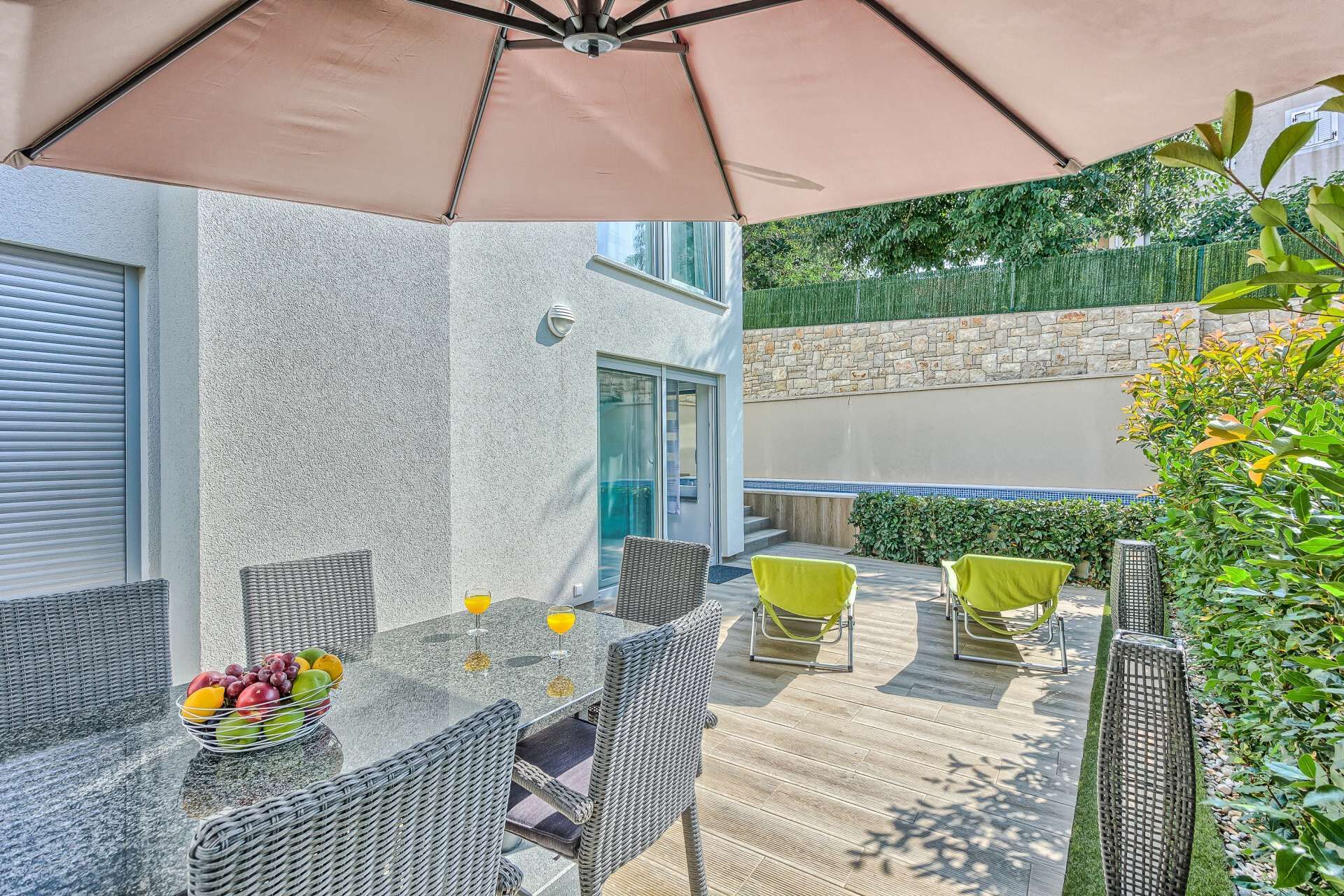 Een terras buiten met rieten meubels, een tafel met fruit en een grote parasol.