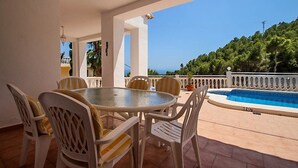 A covered outdoor area with a round table and chairs, a small pool, and a view of a forested hill. - Sesam - sea view villa with private pool in Moraira (Teulada)