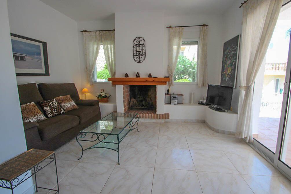 Una sala de estar con sofá, mesa de centro de vidrio, chimenea, televisor y ventanas amplias.