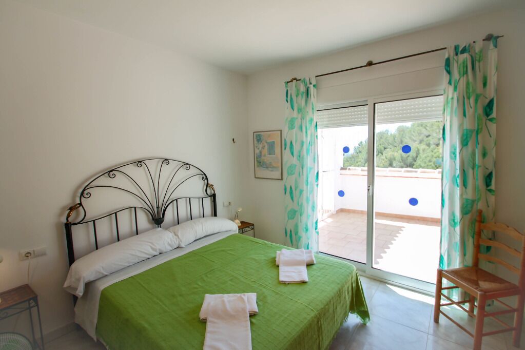 Ein Schlafzimmer mit einem Metallbett, einer grünen Tagesdecke, weißen Kissen und einem Holzstuhl.